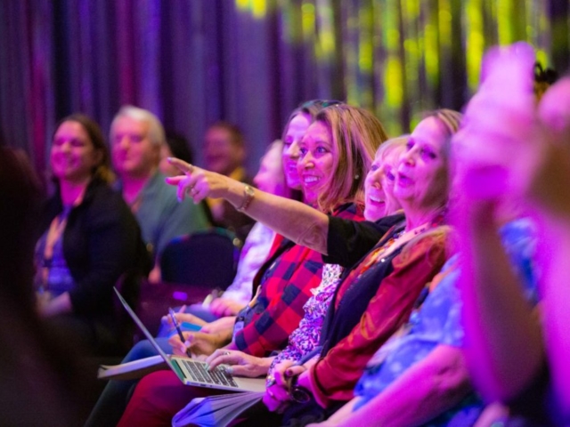 Attendees watch Mark Dawson's keynote at 20Books Vegas as a T Rex waits in the wings.